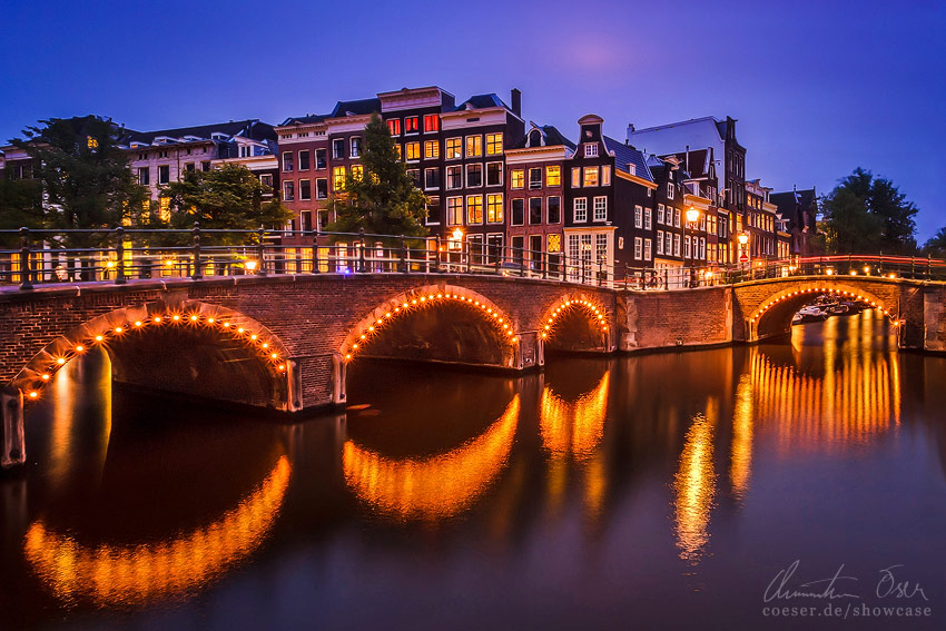 Beleuchtete Keizersgracht und Reguliersgracht während eines Sonnenuntergangs in Amsterdam, Niederlande.