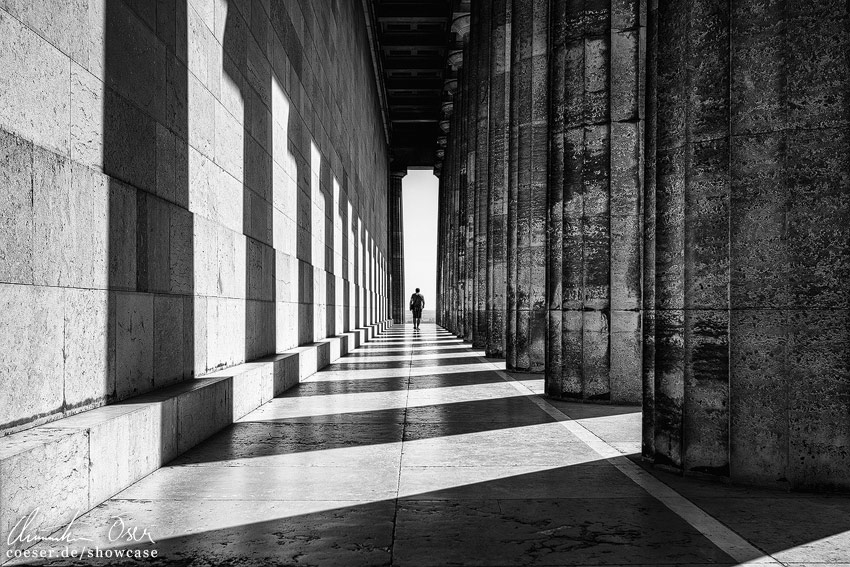 Eine Person zwischen den Schatten werfenden Säulen der Gedenkstätte Walhalla in Regensburg, Deutschland.