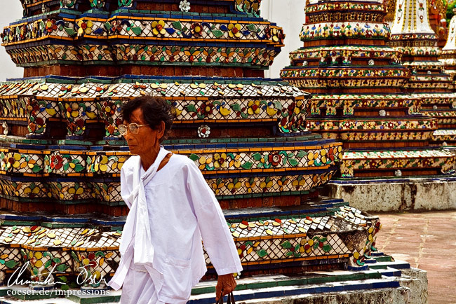 Ein Gläubiger geht an mehreren mosaikgeschmückten Säulen vorbei in Bangkok, Thailand.