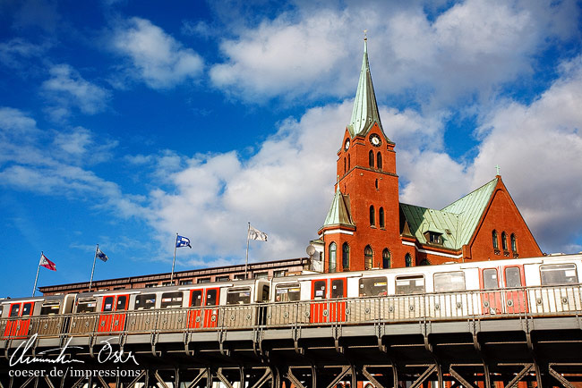 Ein U-Bahn-Zug fährt an der schwedischen Gustaf-Adolfs-Kirche (Gustaf Adolfskyrkan) vorbei in Hamburg, Deutschland.