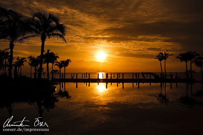 Die aufgehende Sonne und Palmen spiegeln sich in einem Hotel-Swimmingpool in Hua Hin, Thailand.