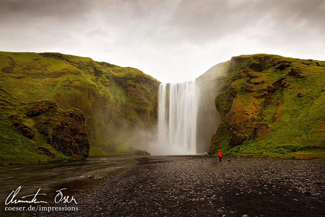 Ein Mann genießt den Skogarfoss-Wasserfall im Regen in Island.