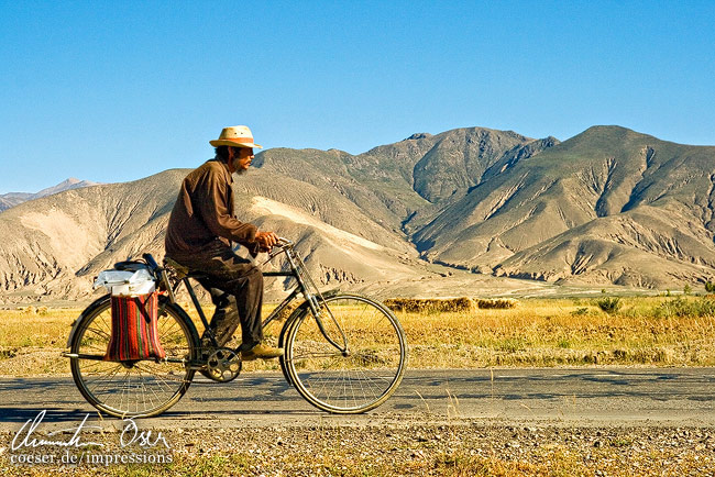 Ein Radfahrer umgeben von Bergen auf einer Straße außerhalb der Stadt in Lhasa, Tibet.