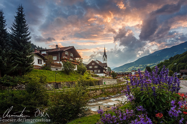 Ansicht des Dorfs Silbertal mit Kirche und dem Litzbach während eines Sonnenuntergangs im Montafon, Vorarlberg, Österreich.