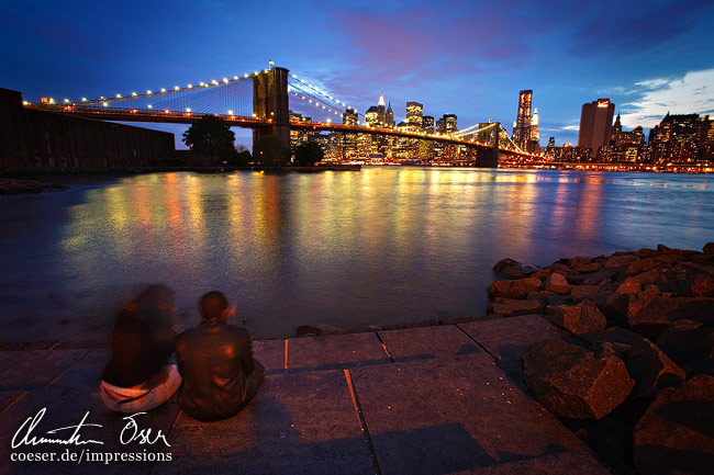 Menschen genießen die beleuchtete Skyline und die Brooklyn Bridge in New York City, USA.