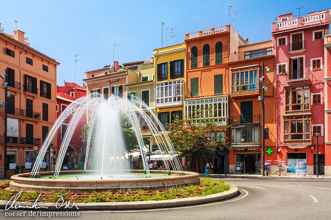 Ein Springbrunnen vor bunten Häusern am Placa de la Reina in Palma de Mallorca, Spanien.