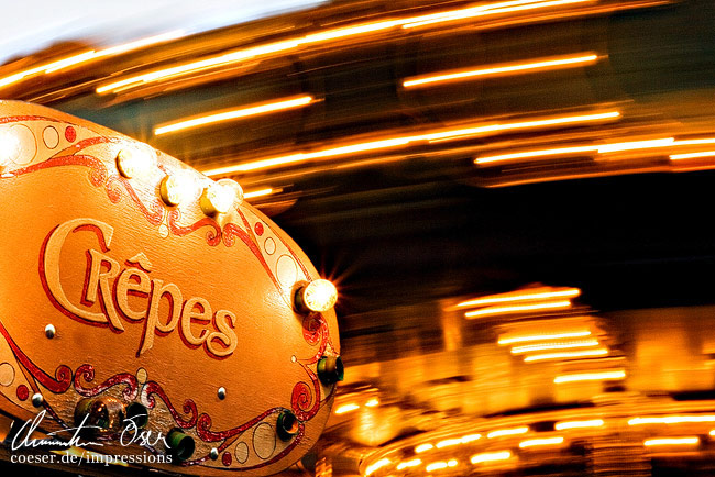 Ein Ringelspiel dreht sich im Hintergrund eines Crepes verkaufenden Standes in Paris, Frankreich.