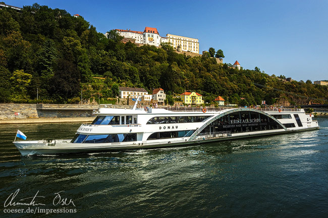 Ein Donaukreuzfahrtschiff vor der Festung Veste Oberhaus in Passau, Deutschland.