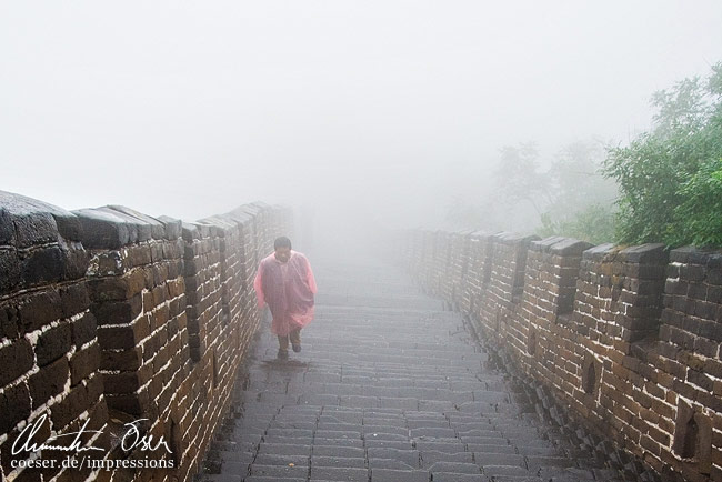 Ein Mann geht in dichtem Nebel die Chinesische Mauer hinauf in Peking, China.