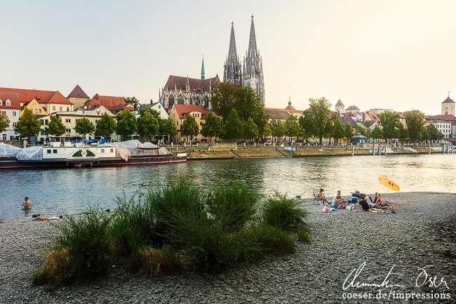 Menschen genießen einen lauen Abend an der Donau vor dem Dom in Regensburg, Deutschland.