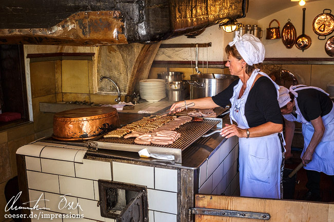 Eine Frau grillt Bratwürste in der historischen Wurstkuchl zu Regensburg, Deutschland.