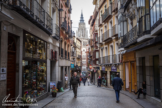 Menschen spazieren durch eine Gasse mit Blick auf die Kathedrale von Toledo, Spanien.